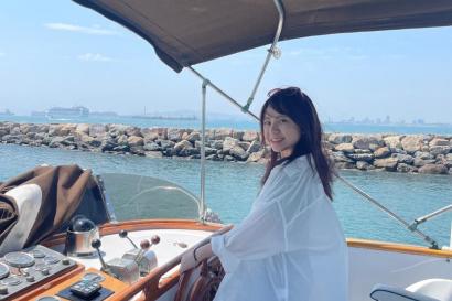 美しい海をバックに小型船のハンドルを握っている写真