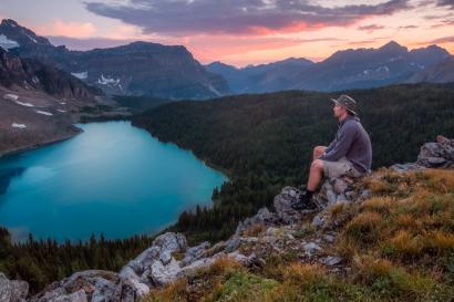 a man sits on a rock overlooking a lake at sunset