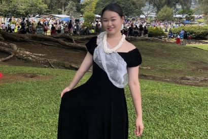木の下で、黒いハワイアンワンピースと首元に白いレイを身に着けた姿