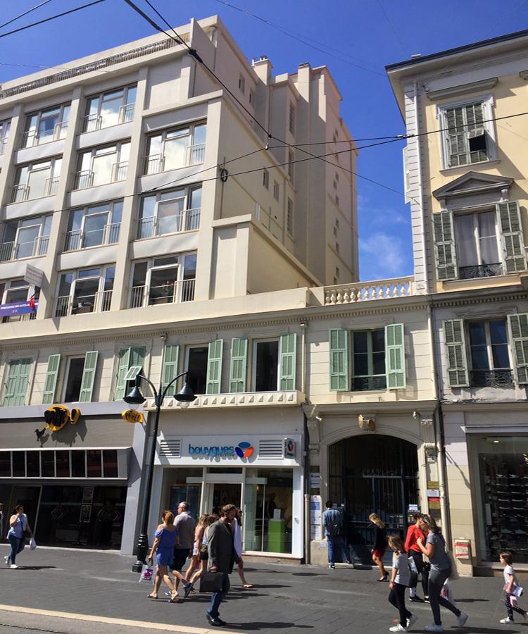 The exterior of a white windowed six story building adjoined to a four story yellow building.