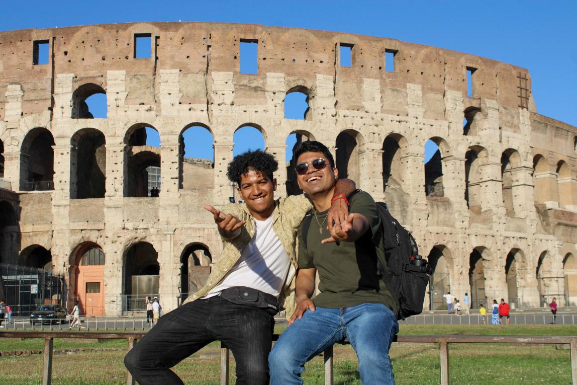 two male students pose for a fun photo in front of the Roman Colosseum in Italy