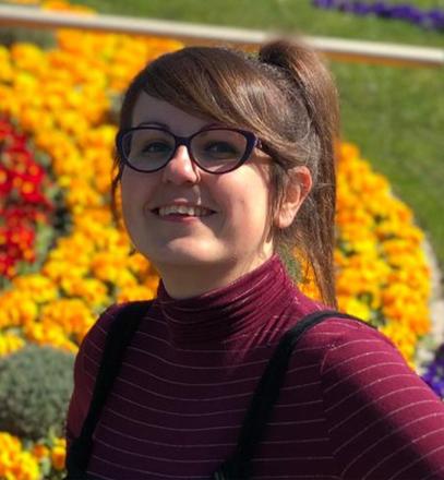 Headshot of Maria Paez Moriana. There are bright yellow flowers in the background.