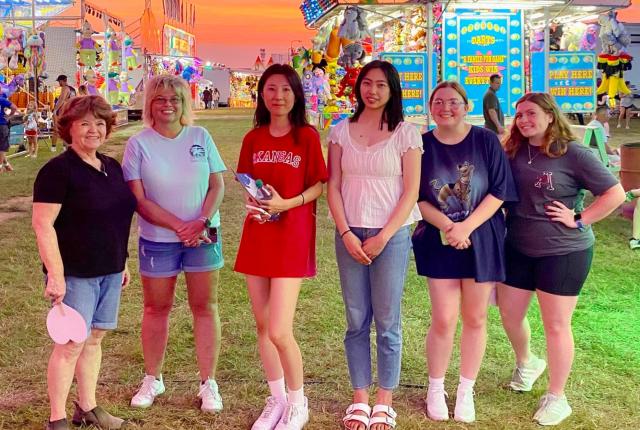 アメリカ、アーカンソー大学のイベントでホストファミリーと友人たちと遊園地へ。背後にはオレンジ色の美しい夕焼けと様々な出店。