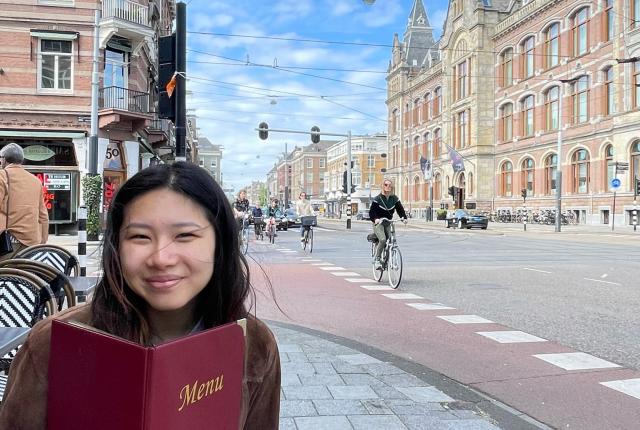 a student sitting on an outdoor restaurant patio with a menu in Amsterdam