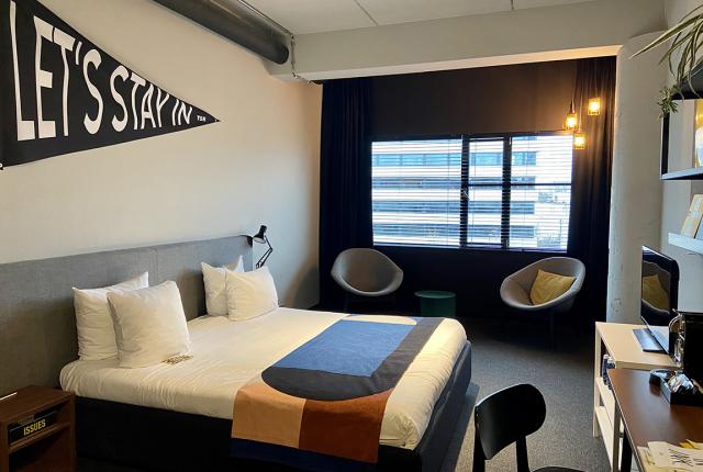 A clean bedroom with a window, modern chairs, a bed, a desk, and a television.