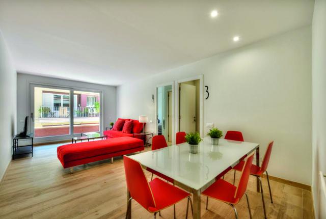 A minimalist living space featuring bright red furniture, a large window, a television, and a dining room with red chairs.