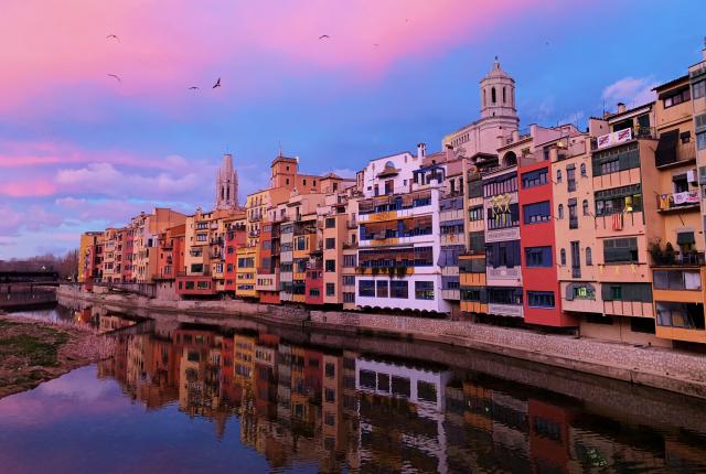 multicolored buildings bordering a lake with pink clouds and a blue sky