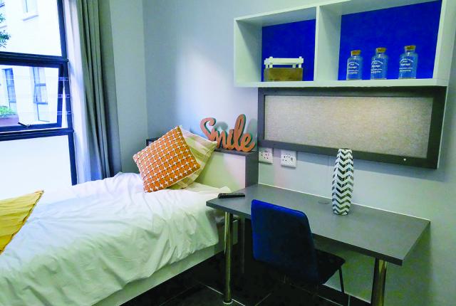 A clean bedroom featuring a twin-sized bed, a desk, and shelving with bright blue backings.