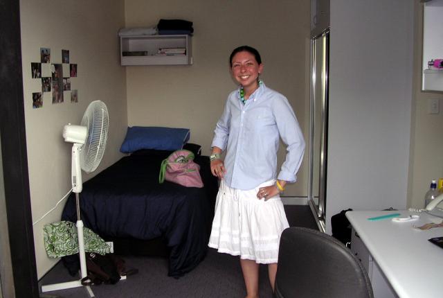 A student stands in their UNSW Shalom College student room, with a bed, a desk, and a bathroom.