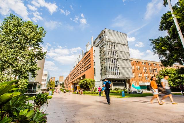在新南威尔士大学的校园，学生们走在上课路上，主干道两旁坐落着高大的砖砌建筑。
