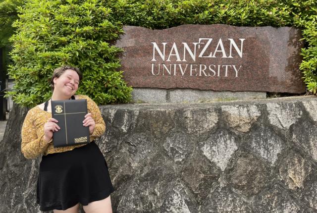 Author, Macks, standing with diploma in front of Nanzan University's sign.