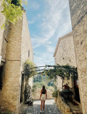 A students stands between two buildings in Nice, France. In front of her are trees.